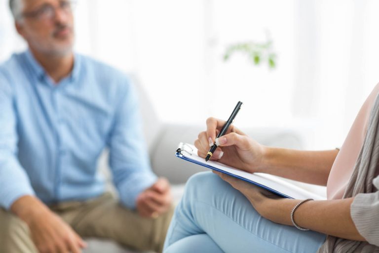 Female doctor writing on clipboard while consulting a man at home